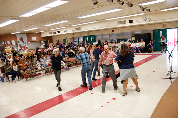 A group of older adults perform a dance in the cafeteria for families