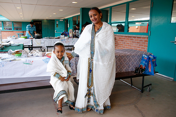 A little girl and her mom smile, dressed in traditional white robes