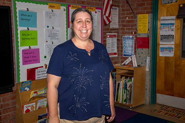 A woman in a navy blue shirt smiles in front of boards in her classroom