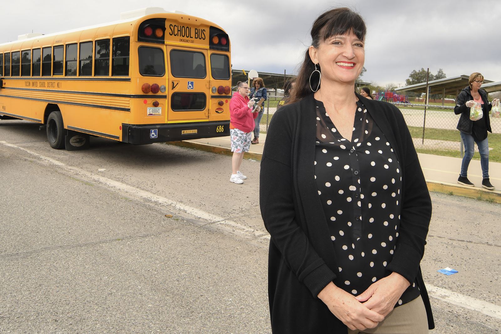 Principal Megan Stefanek in front of Myers Ganoung School and bus with students walking by.